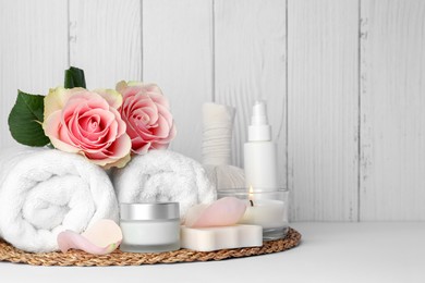 Photo of Composition with different spa products, roses and candle on white table against wooden background. Space for text