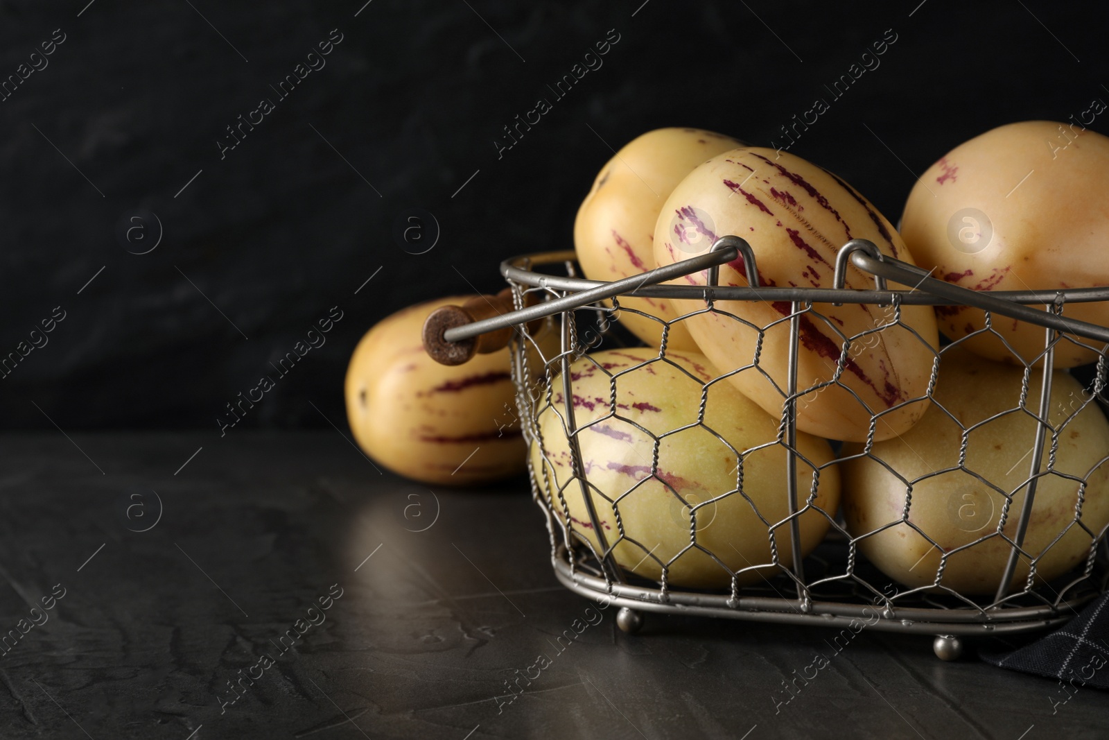 Photo of Fresh ripe pepino melons in metal basket on black table, space for text