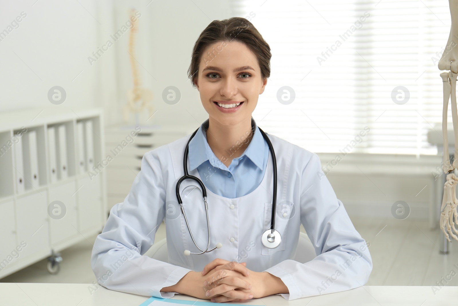 Photo of Female orthopedist at table near human skeleton model in office