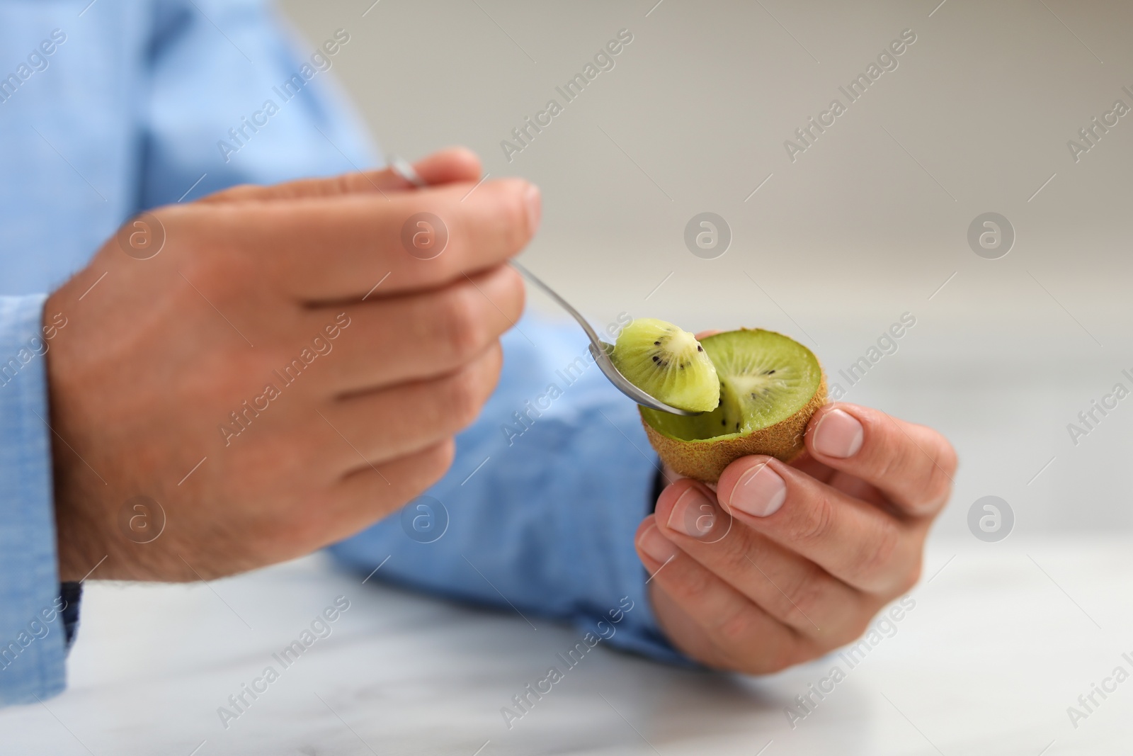 Photo of Man eating kiwi with spoon at white table, closeup