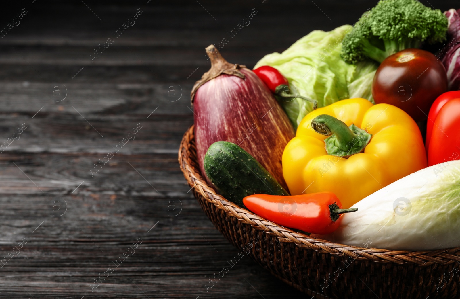 Photo of Fresh vegetables in wicker bowl on black wooden table, closeup