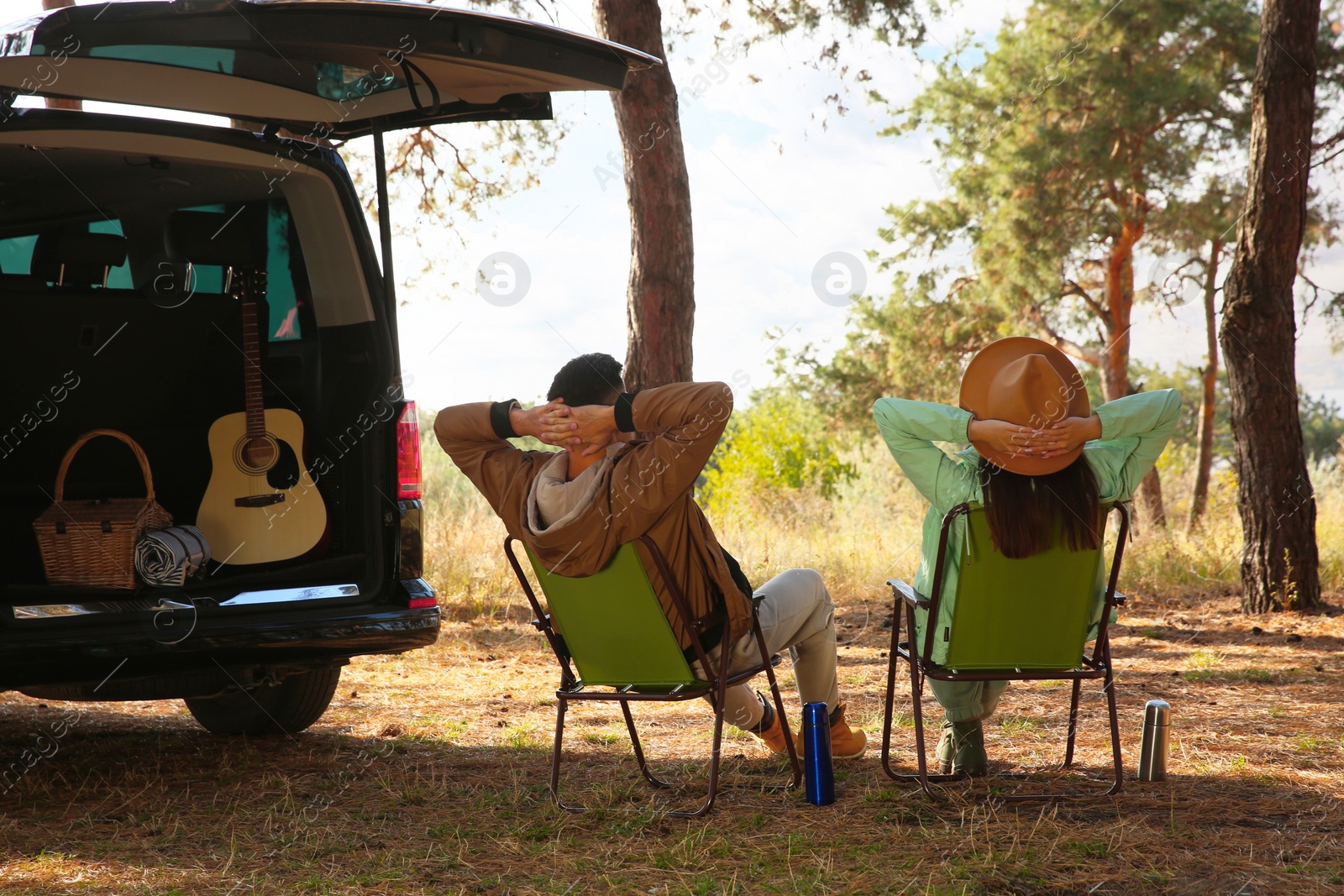 Photo of Couple with thermoses resting in camping chairs on autumn day, back view