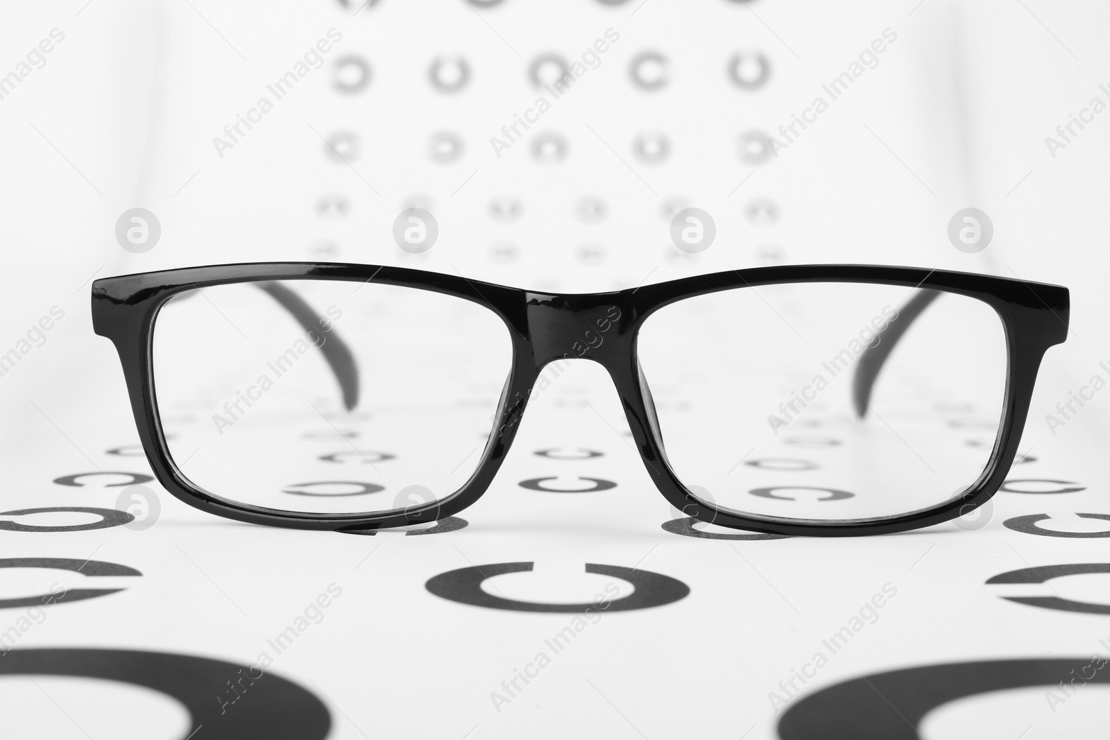 Photo of Vision test chart and glasses on white background, closeup