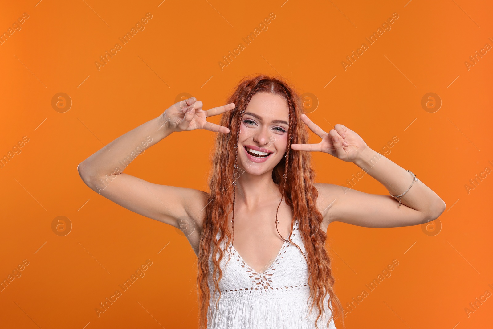 Photo of Beautiful young hippie woman showing V-sign on orange background