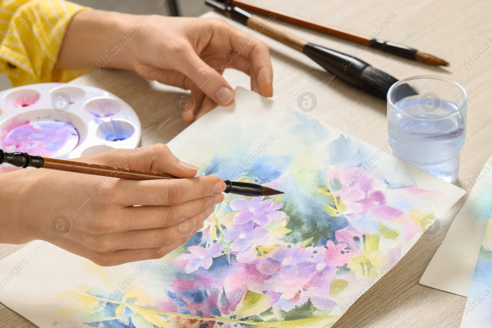 Photo of Woman painting flowers with watercolor at white wooden table, closeup. Creative artwork