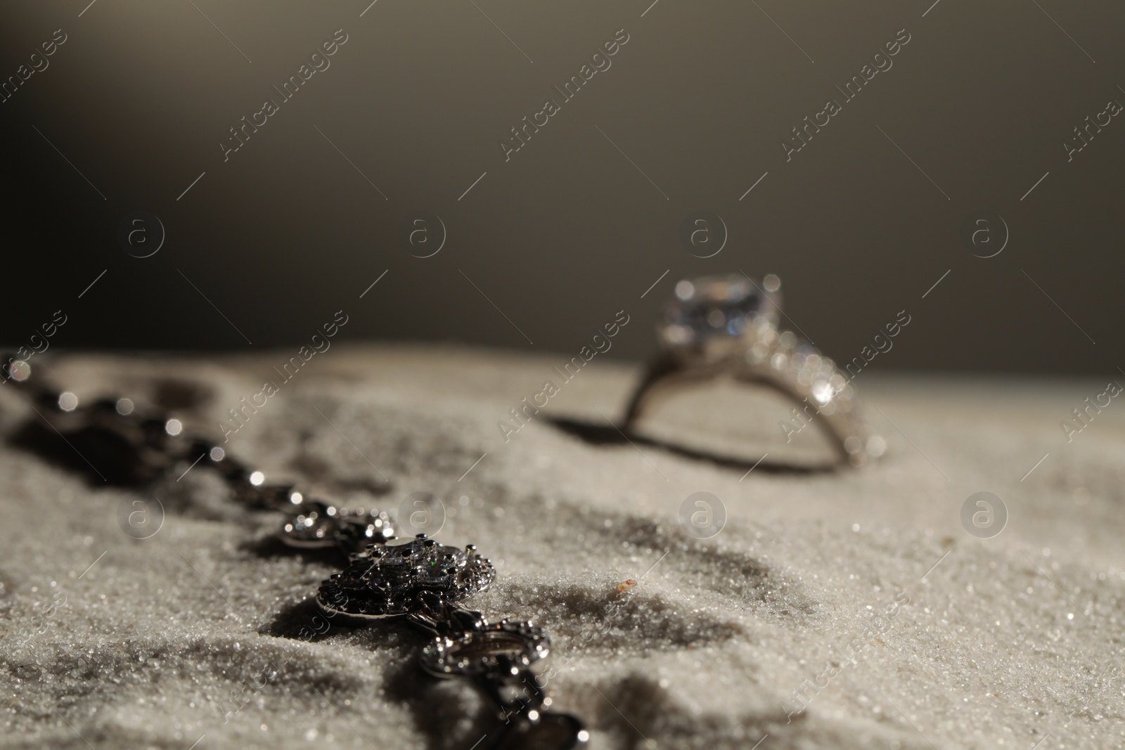 Photo of Luxury jewelry. Stylish presentation of bracelet and ring on sand against grey background, space for text