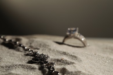 Photo of Luxury jewelry. Stylish presentation of bracelet and ring on sand against grey background, space for text