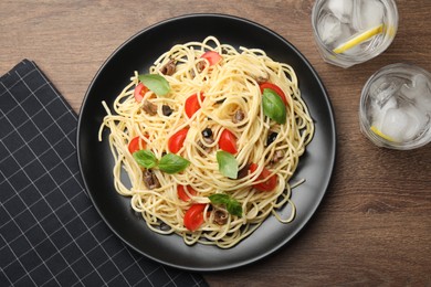 Photo of Delicious pasta with anchovies, tomatoes and glasses of beverage on wooden table, flat lay