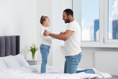 Photo of Little girl with her father spending time together on bed at home. International family