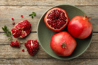 Photo of Fresh pomegranates and green leaves on wooden table, flat lay
