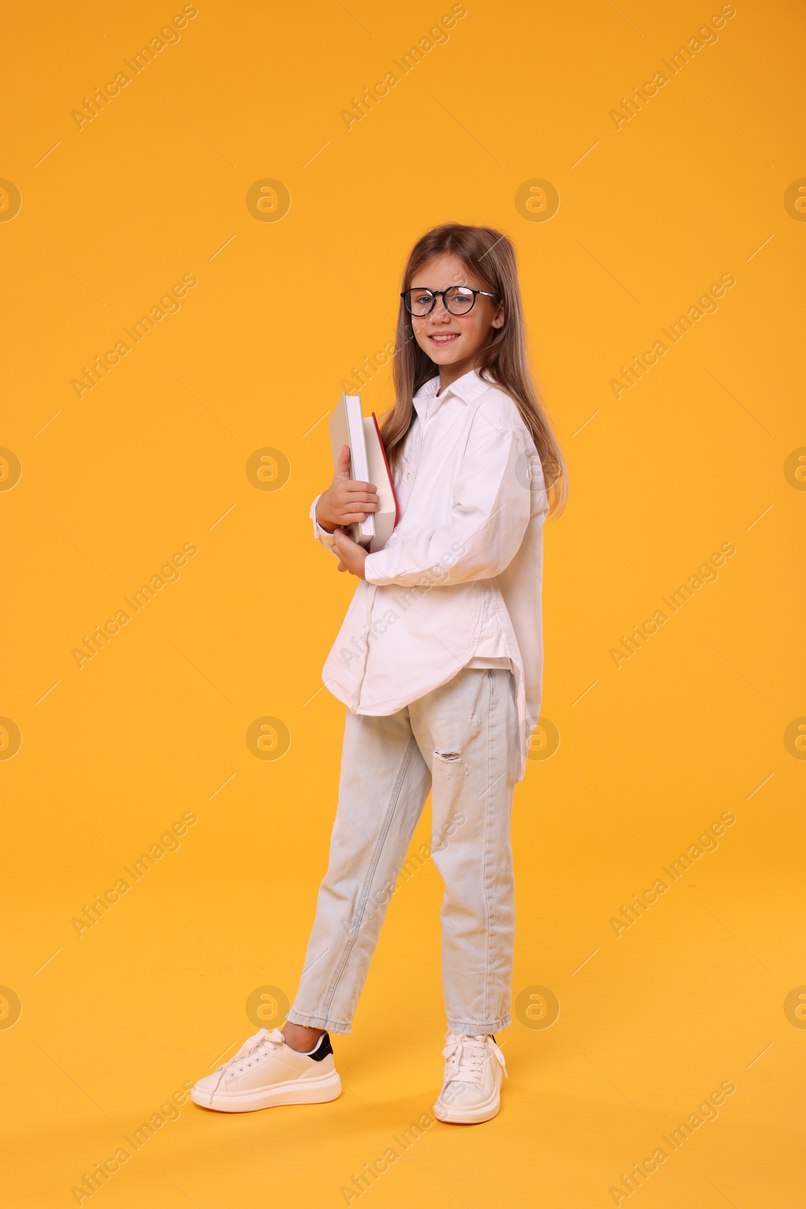 Photo of Happy schoolgirl with books on orange background