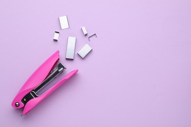 Photo of New bright stapler with staples on violet background, fat lay. Space for text
