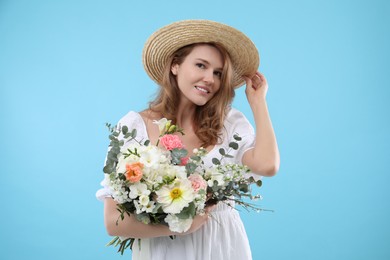 Beautiful woman in straw hat with bouquet of flowers on light blue background