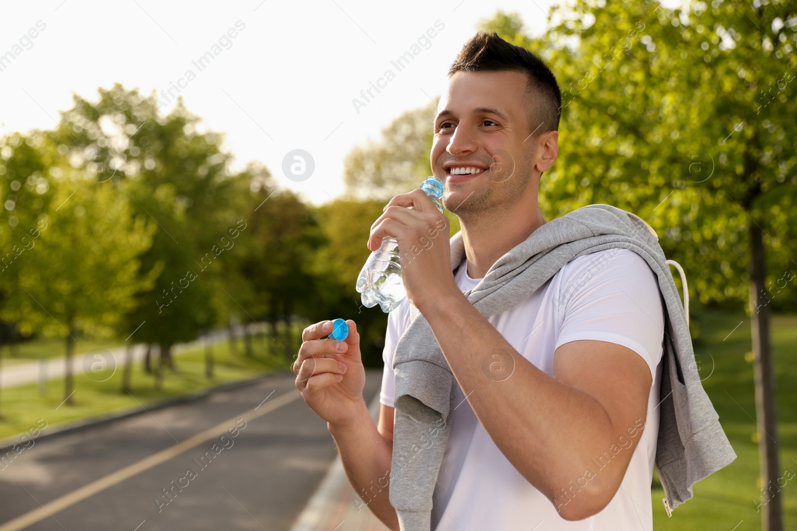 Photo of Young man drinking water outdoors. Morning fitness