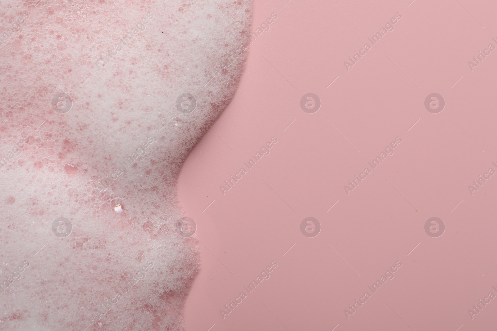 Photo of Fluffy soap foam on pink background, top view. Space for text