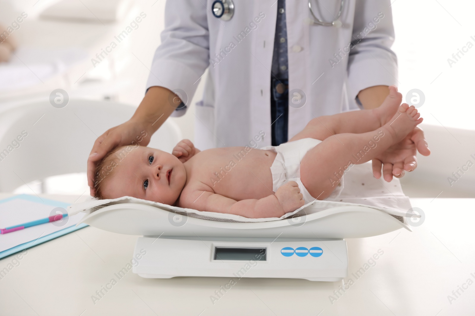 Photo of Doctor weighting cute baby in clinic, closeup. Health care