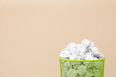 Metal bin with crumpled paper against color background, space for text