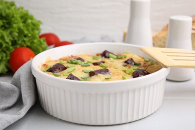 Photo of Tasty sausage casserole with green onions in baking dish served on white tiled table, closeup