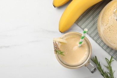Photo of Mason jar of tasty banana smoothie with straw and fresh fruits on white marble table, flat lay. Space for text