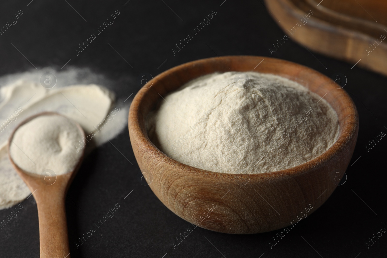 Photo of Bowl and spoon of agar-agar powder on black background, closeup