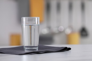 Photo of Glass of water and napkin on white table against blurred background. Space for text