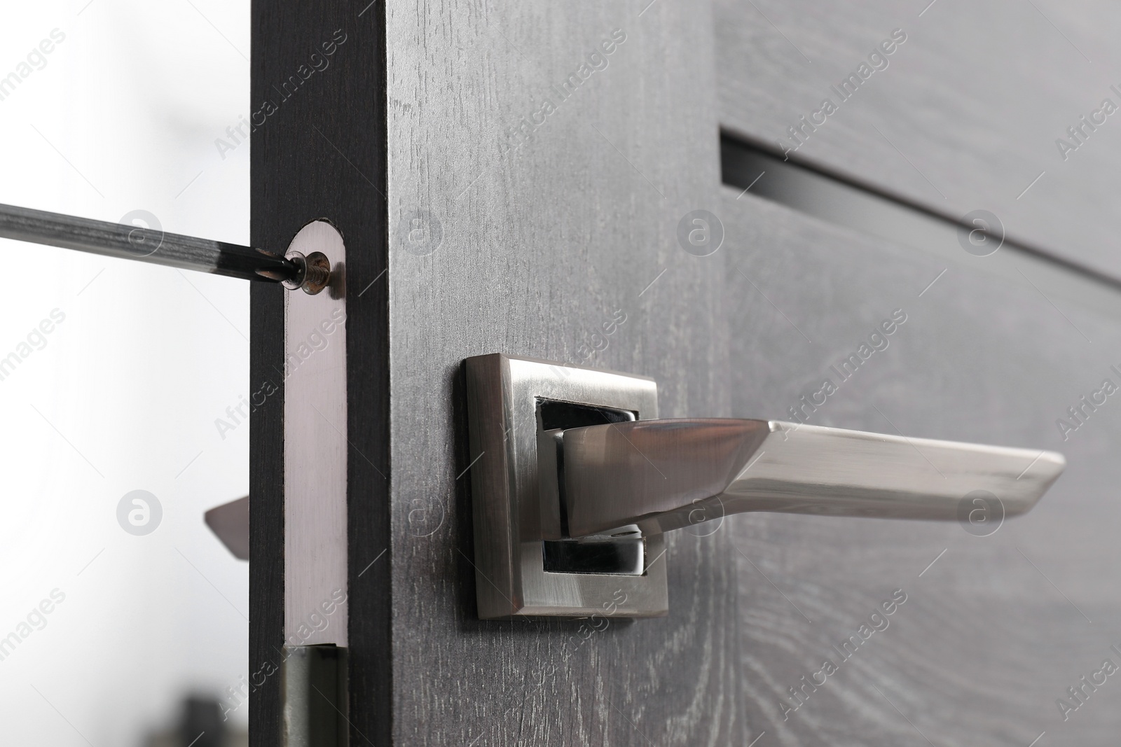 Photo of Repairing door handle with screwdriver indoors, closeup