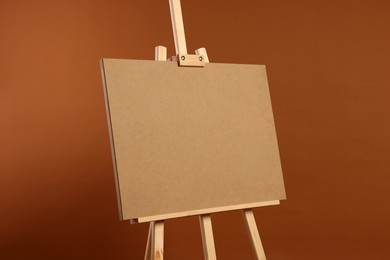Wooden easel with blank board on brown background