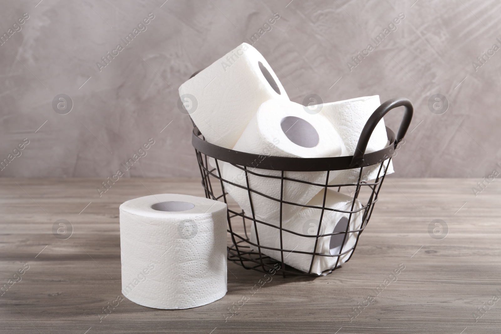 Photo of Soft toilet paper rolls in metal basket on wooden table, closeup