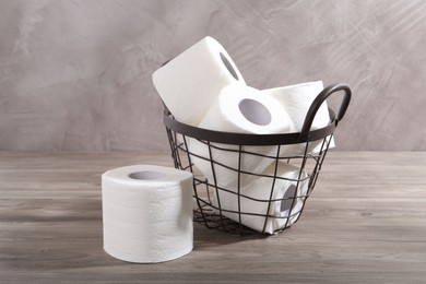 Photo of Soft toilet paper rolls in metal basket on wooden table, closeup