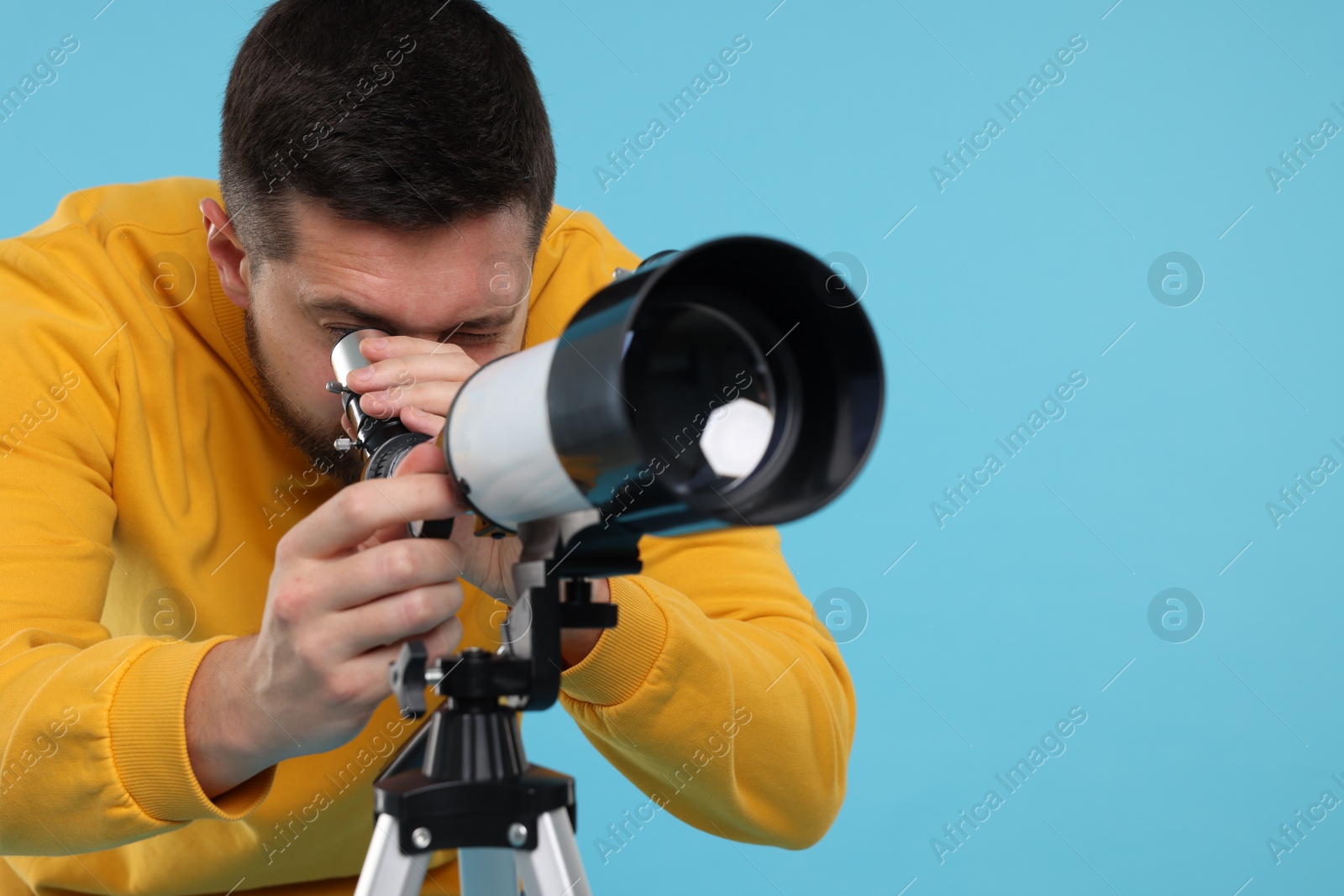 Photo of Astronomer looking at stars through telescope on light blue background. Space for text