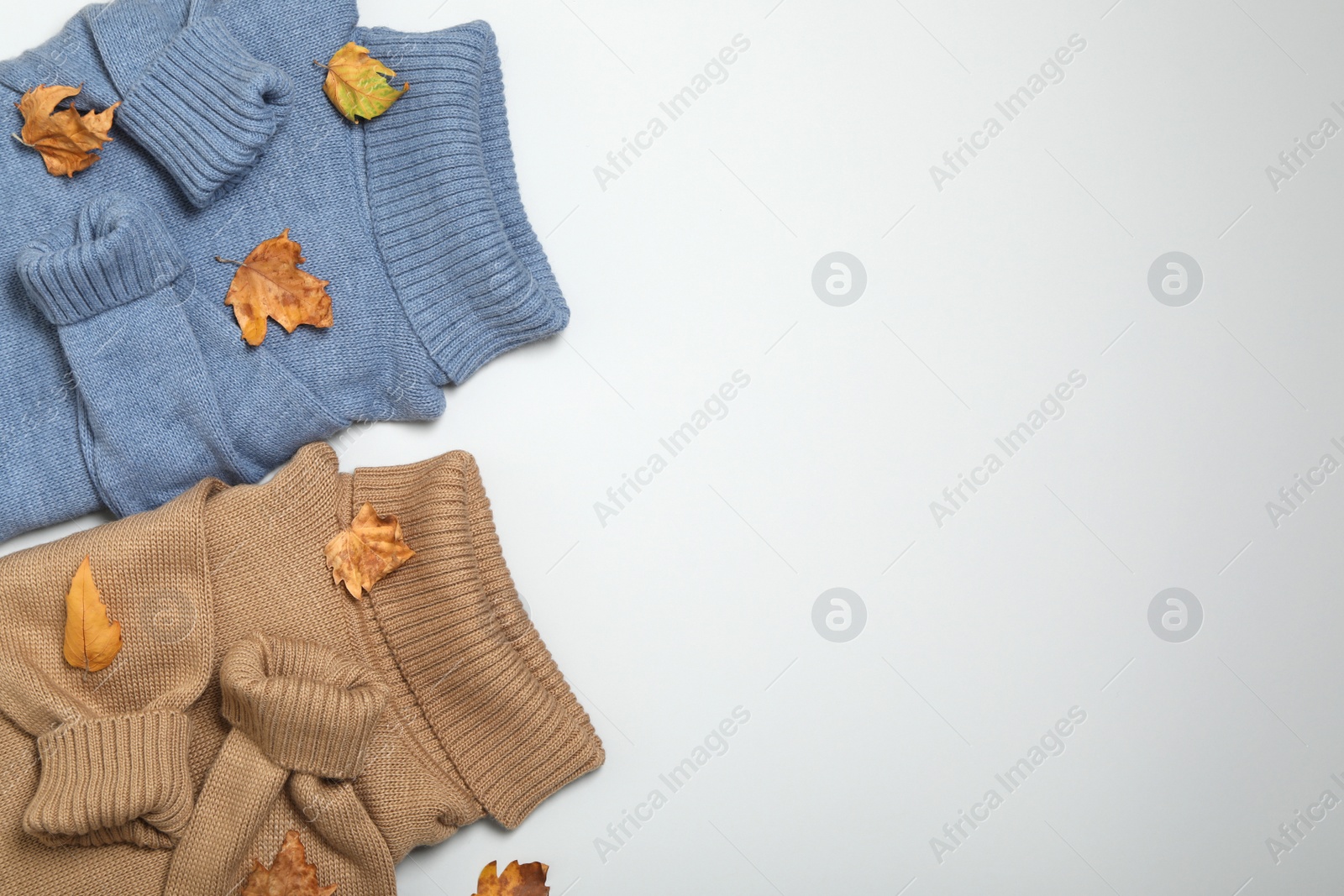Photo of Warm sweaters and dry leaves on white background, top view with space for text. Autumn season