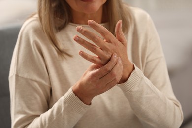 Photo of Mature woman suffering from pain in hand on blurred background, closeup. Rheumatism symptom