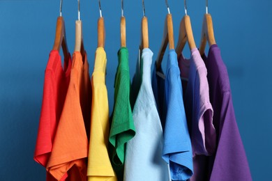 Photo of Bright clothes on wooden hangers against blue background. Rainbow colors