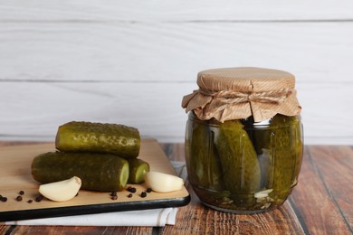 Jar with tasty pickled cucumbers and ingredients on wooden table