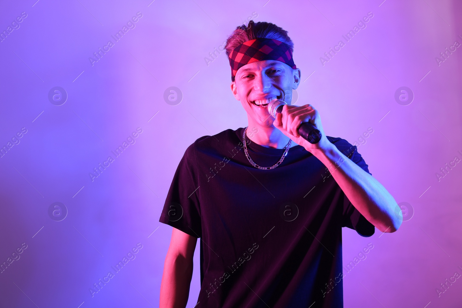 Photo of Stylish young man singing on color background in neon lights