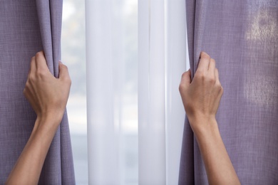 Photo of Woman opening window curtains at home, closeup. Space for text