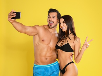 Photo of Young attractive couple in beachwear taking selfie on yellow background