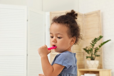 Photo of Cute African-American girl with toothbrush on blurred background