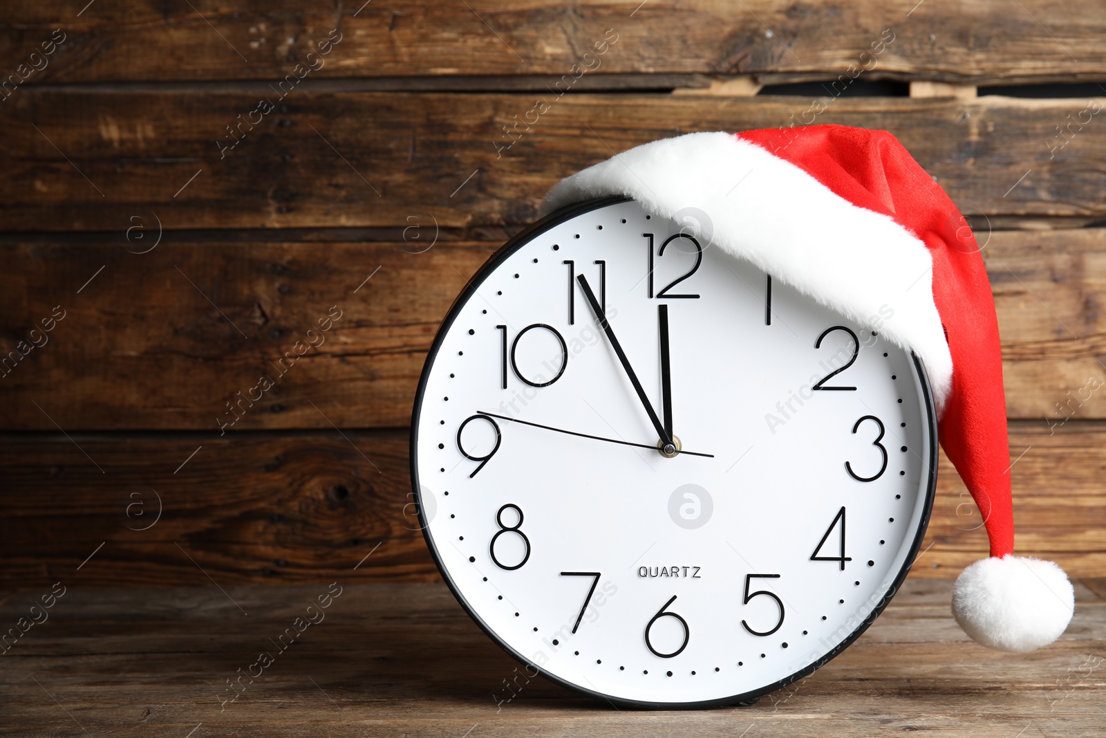 Photo of Clock with Santa hat showing five minutes until midnight on wooden background, space for text. New Year countdown