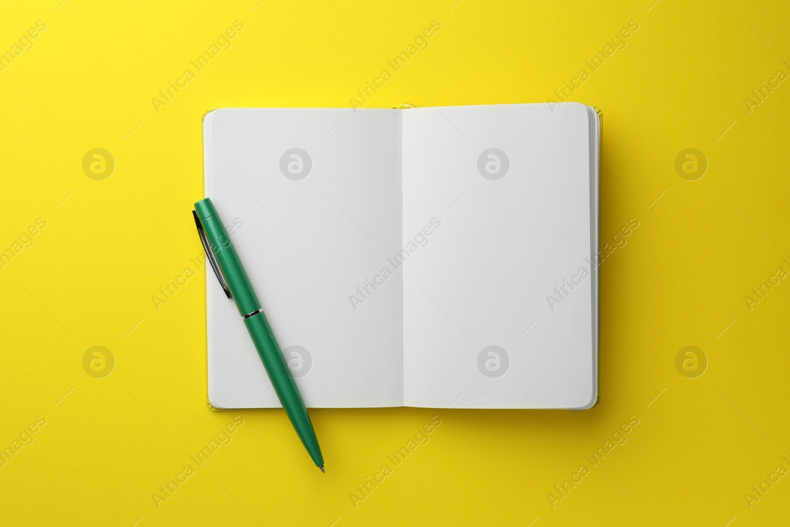 Photo of Open notebook with blank pages and pen on yellow background, top view. Space for text