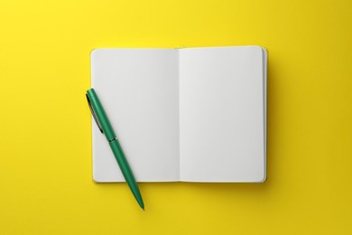 Photo of Open notebook with blank pages and pen on yellow background, top view. Space for text