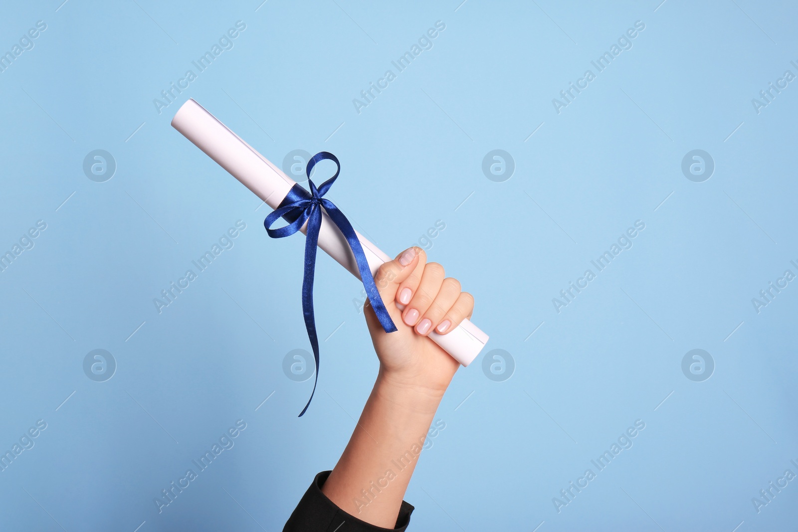 Photo of Student holding rolled diploma with ribbon on light blue background, closeup