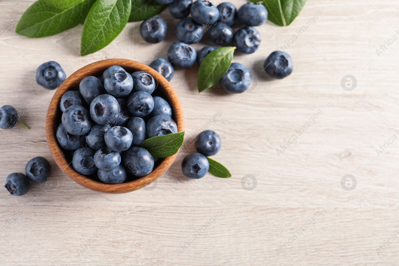 Photo of Bowl of fresh tasty blueberries with leaves on white wooden table, flat lay. Space for text