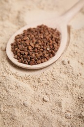 Spoon with buckwheat grains on flour, closeup