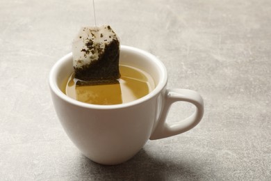 Taking tea bag out of cup with hot beverage at light table, closeup. Space for text