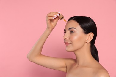 Photo of Young woman applying essential oil onto face against pink background