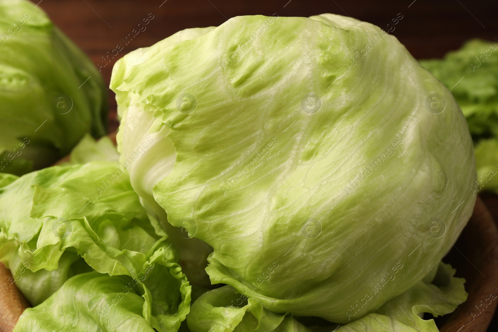 Photo of Fresh green iceberg lettuce heads and leaves in wooden bowl, closeup