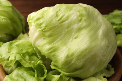 Fresh green iceberg lettuce heads and leaves in wooden bowl, closeup