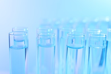 Photo of Many glass test tubes on light blue background, closeup