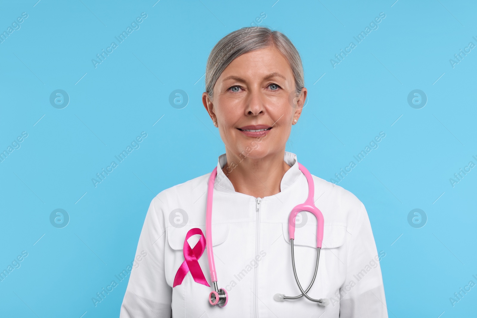 Photo of Doctor with pink ribbon and stethoscope on light blue background. Breast cancer awareness